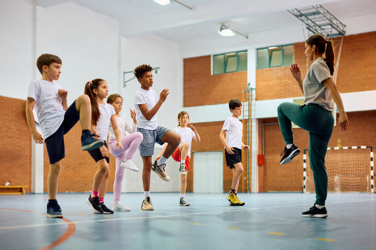 School kids and sports teacher exercising during PE class at school gym.